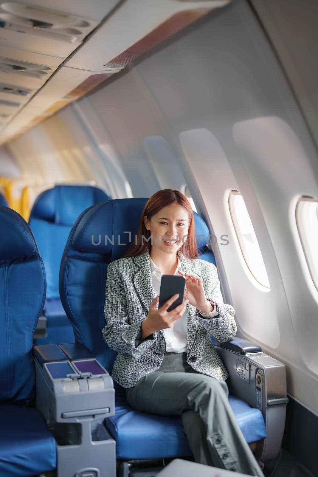 portrait of A successful asian businesswoman or female entrepreneur in formal suit in a plane sits in a business class's seat and uses a smartphone during flight.