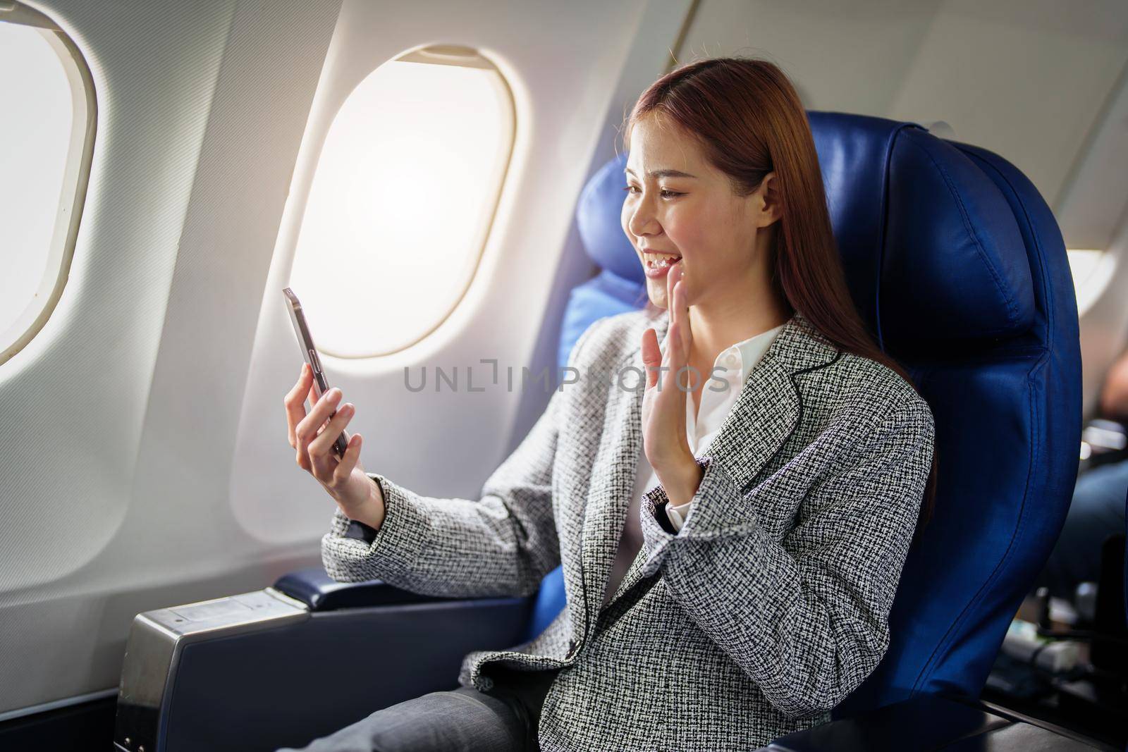 portrait of A successful asian businesswoman or female entrepreneur in formal suit in a plane sits in a business class's seat and uses a smartphone during flight.
