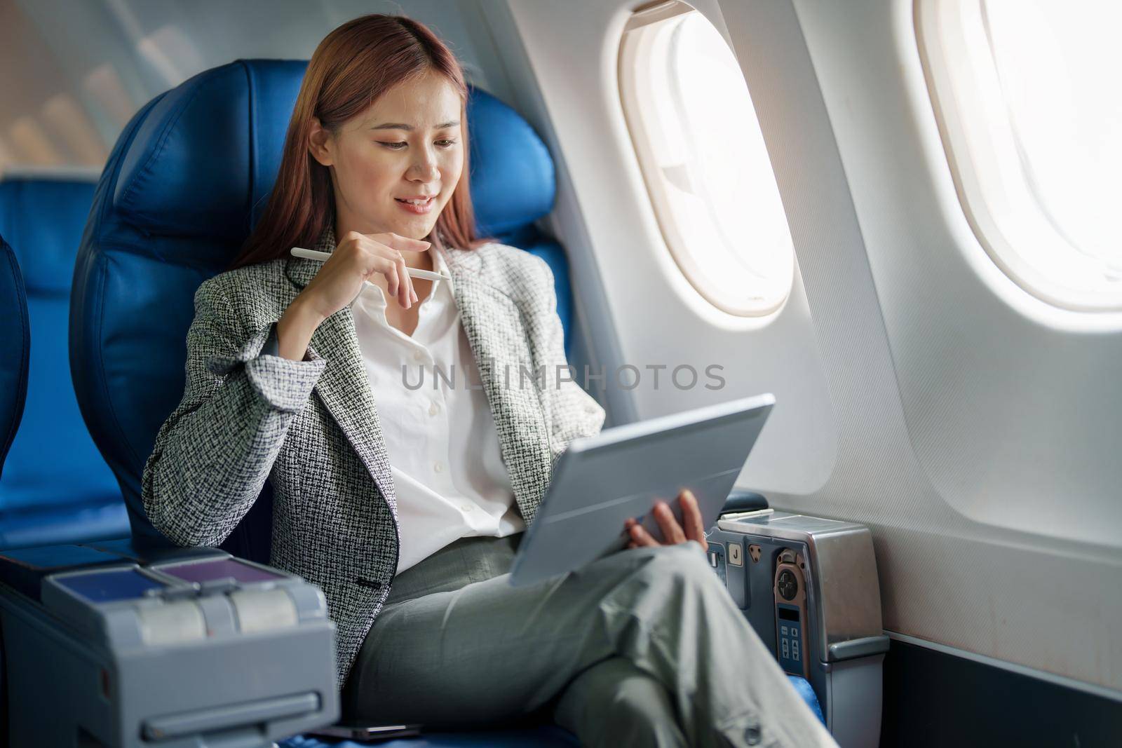 portrait of A successful asian businesswoman or female entrepreneur in formal suit in a plane sits in a business class's seat and uses a tablet computer during flight.
