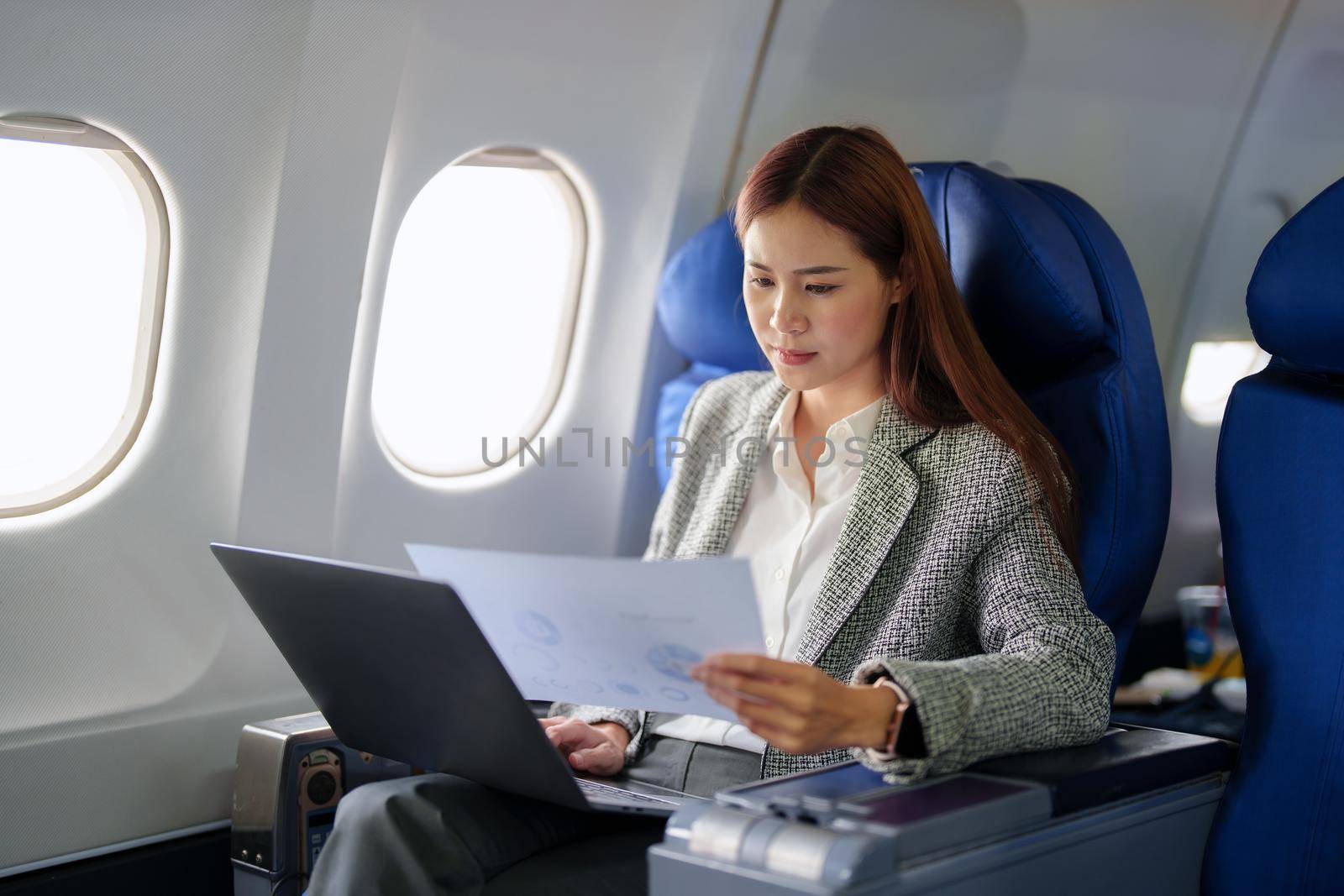 portrait of A successful asian business woman or female entrepreneur in formal suit in a plane sits in a business class seat and uses a documents with computer laptop during flight.