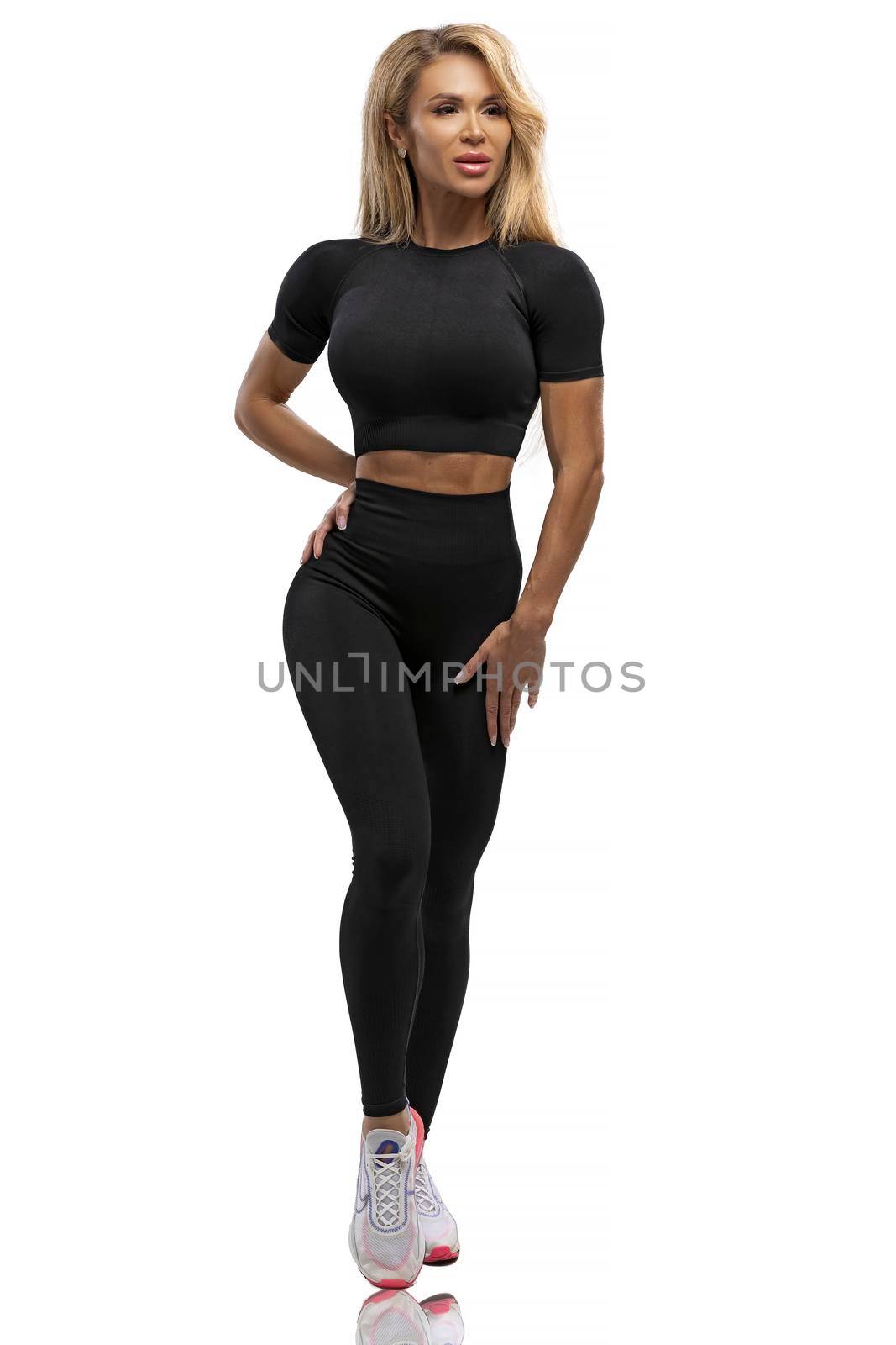 Blonde fit girl in leggings and top on a white background in the studio by but_photo