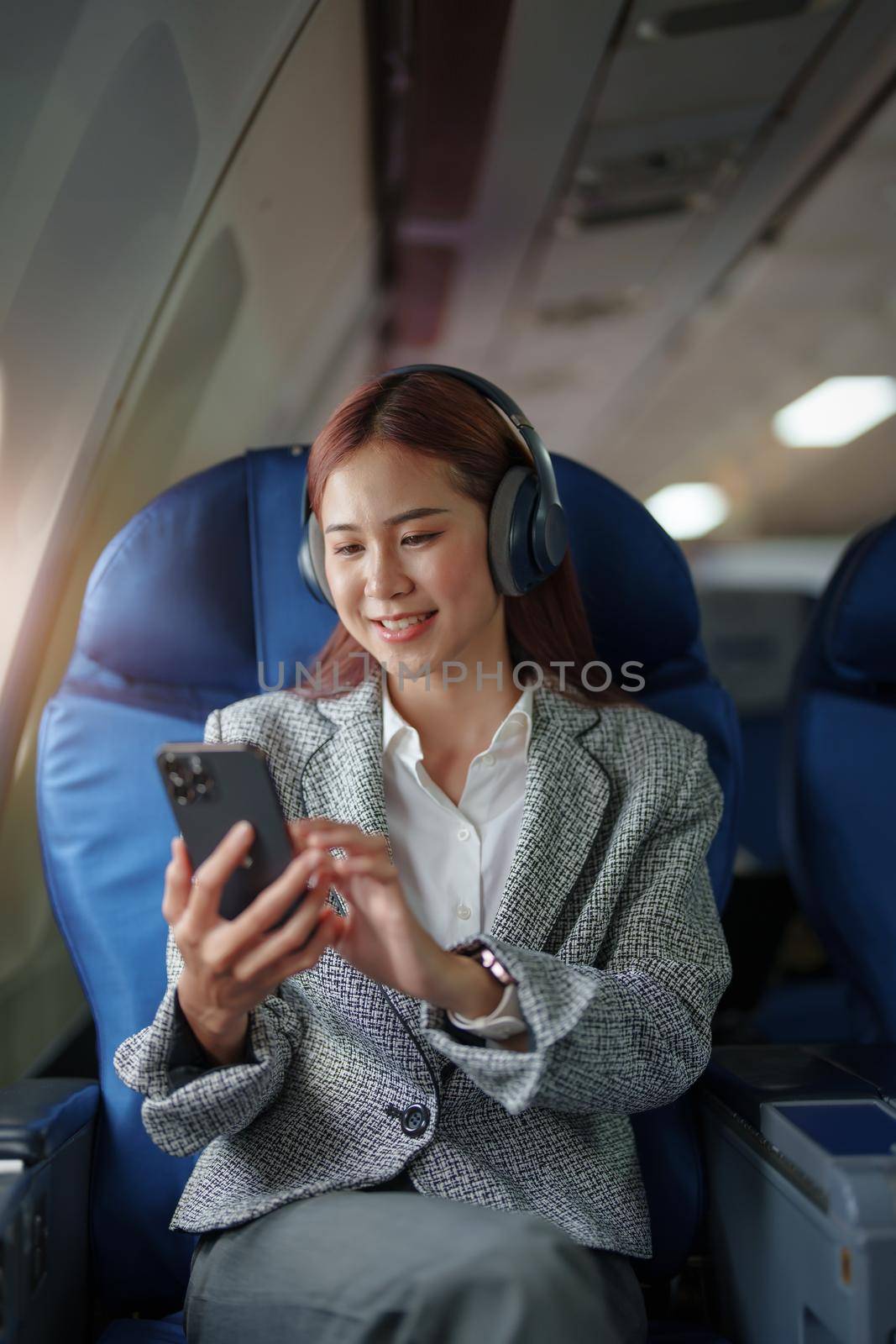 portrait of A successful asian business woman in a plane sits in a business class seat and uses a smartphone for playing music during flight, relex concept by Manastrong