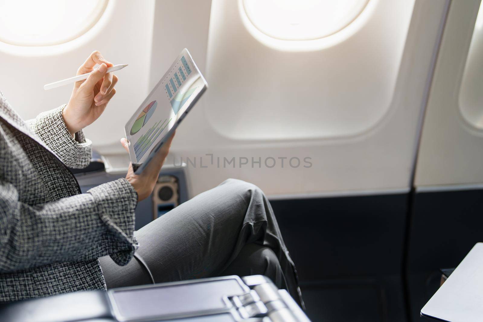 A successful asian businesswoman or female entrepreneur in formal suit in a plane sits in a business class's seat and uses a tablet computer during flight.
