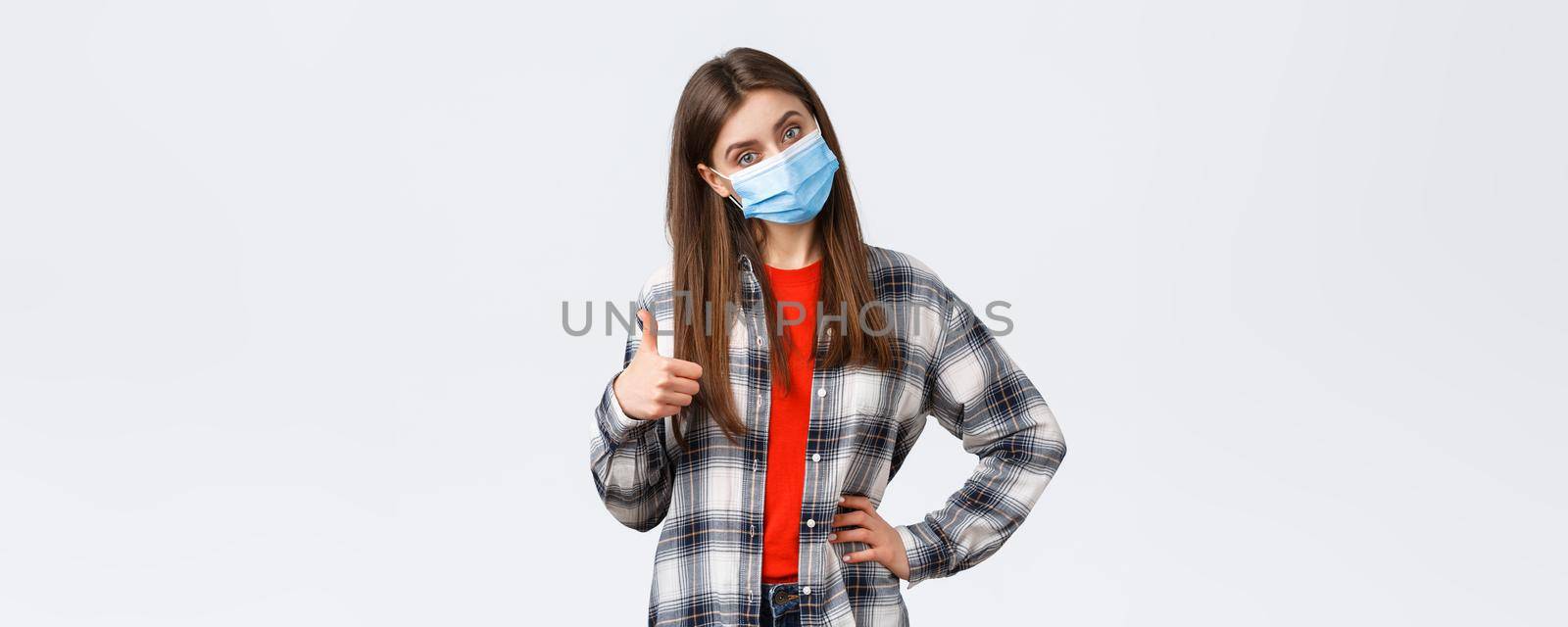 Coronavirus outbreak, leisure on quarantine, social distancing and emotions concept. Confident good-looking woman in medical mask give advice, recommend promo, show thumb-up in approval by Benzoix