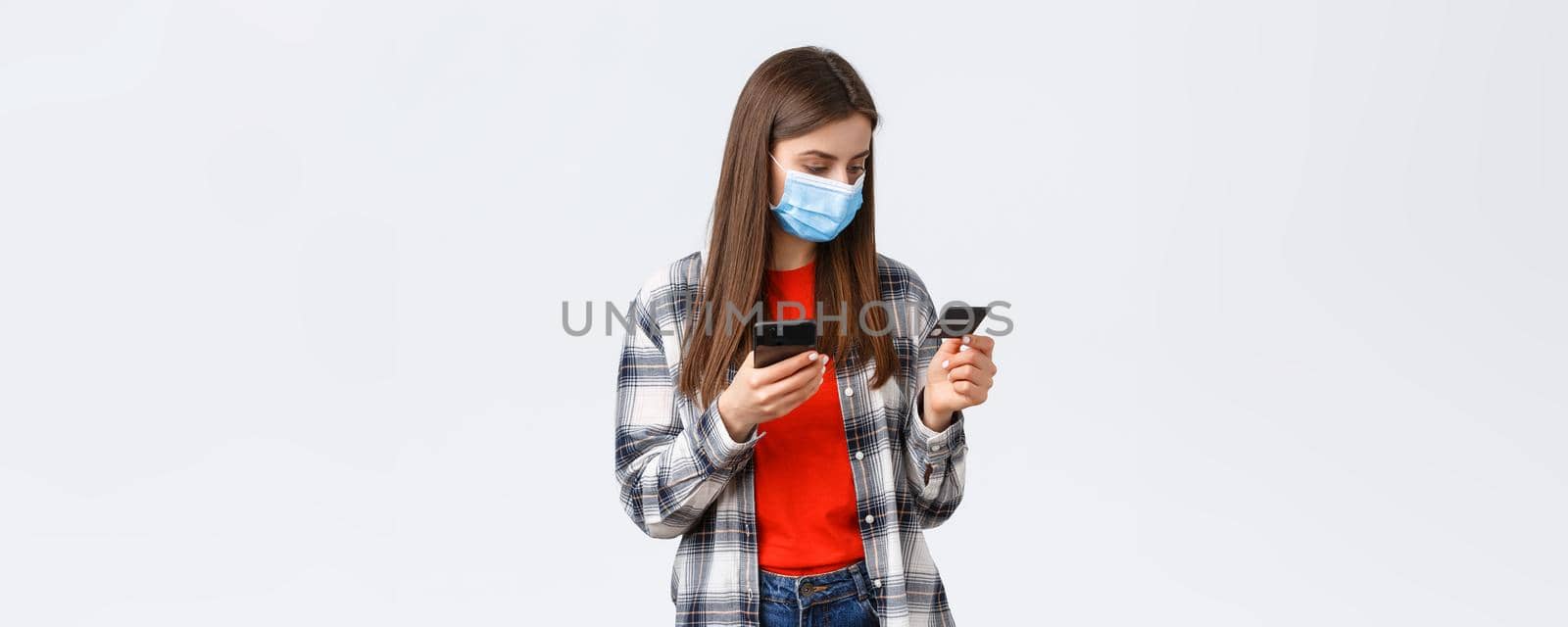 Coronavirus outbreak, working from home, online shopping and contactless payment concept. Girl in medical mask pay order groceries from grocery store to deliver, hold mobile phone and credit card by Benzoix