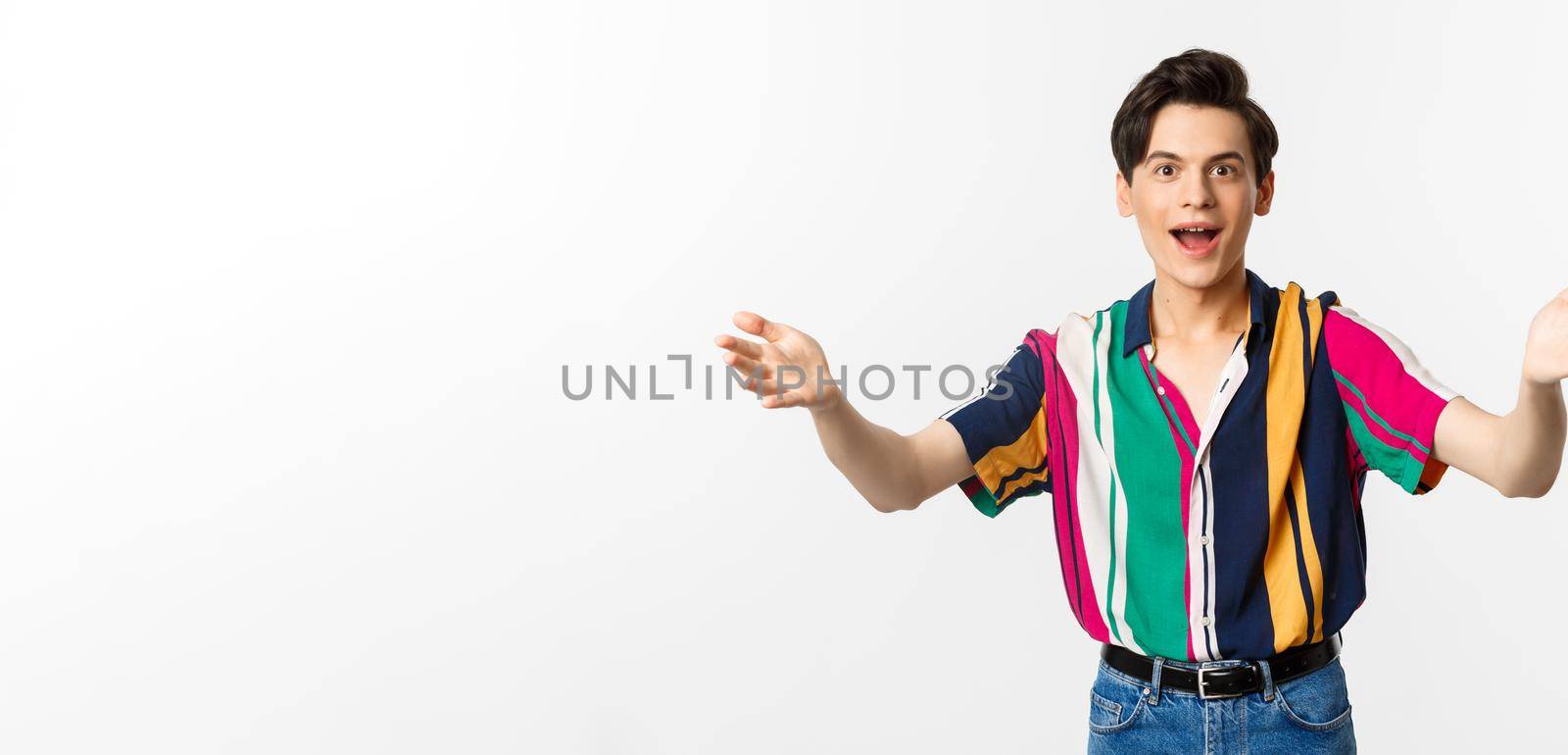 Amazed young handsome man reaching hands forward, want to hold or take something, looking with desire, standing over white background.