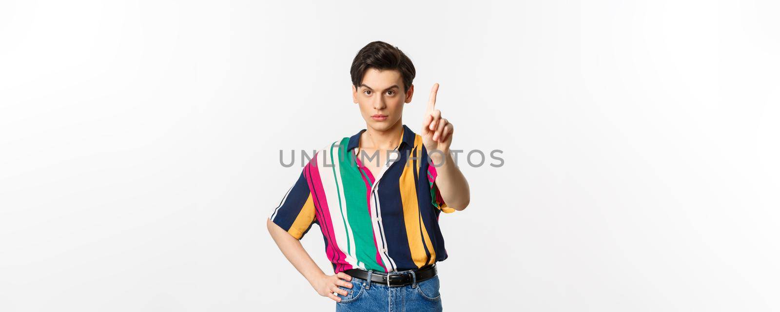 Disappointed young man prohibit something, shaking finger in disapproval, forbid you, standing over white background by Benzoix