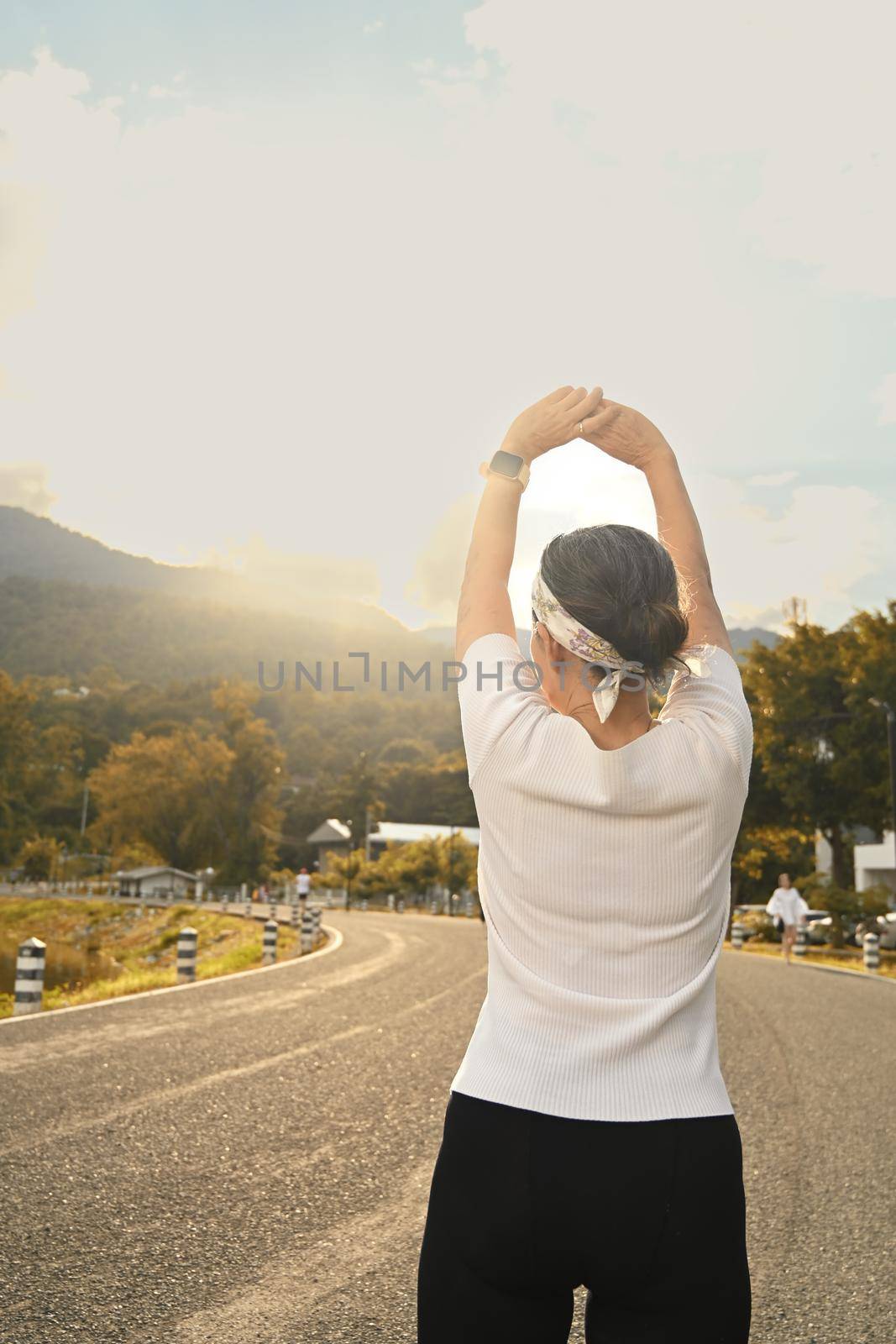 Back view of middle aged woman warming up before morning workout. Healthy lifestyle, workout and wellness concept by prathanchorruangsak