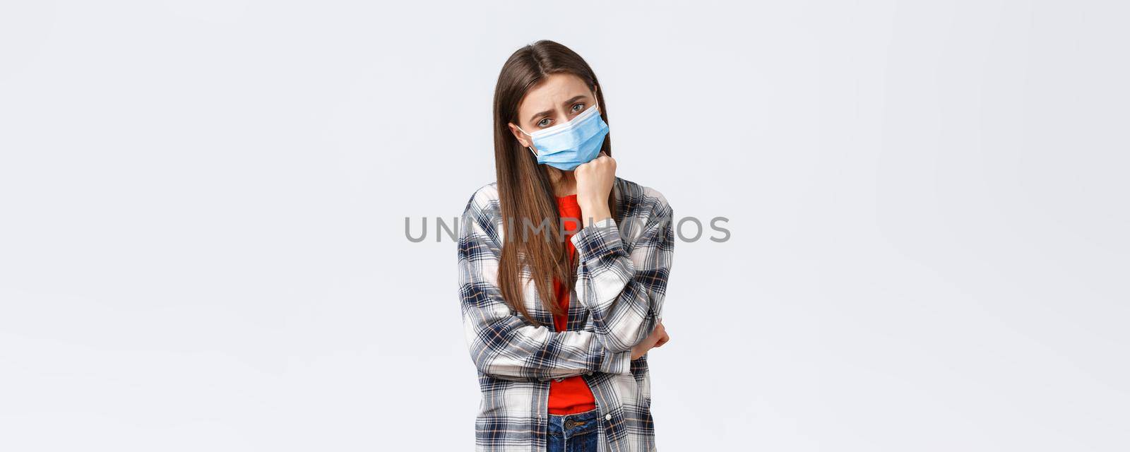 Coronavirus outbreak, leisure on quarantine, social distancing and emotions concept. Sad and bored young gloomy girl in medical mask lean on hand and looking unamused camera.