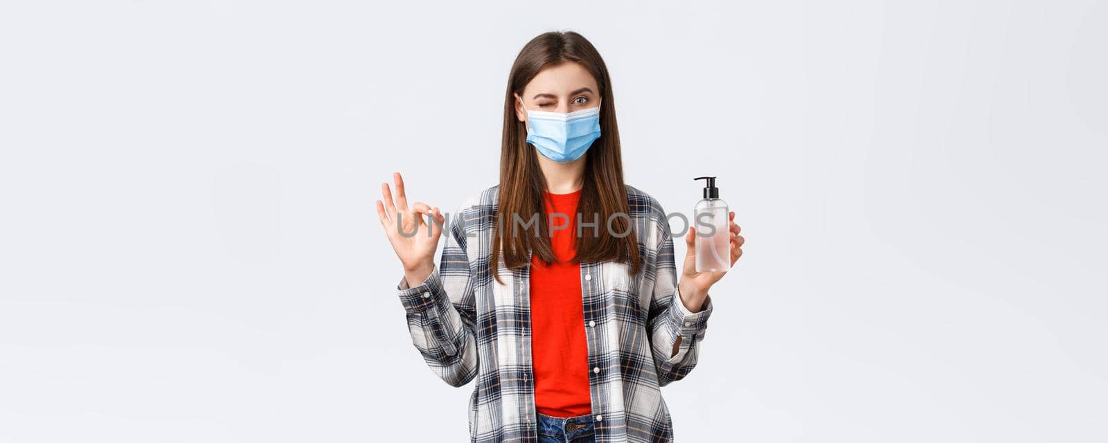 Coronavirus outbreak, leisure on quarantine, social distancing and emotions concept. No problem. Pleased cute girl in medical mask show okay sign and wink as advertise hand sanitizer by Benzoix