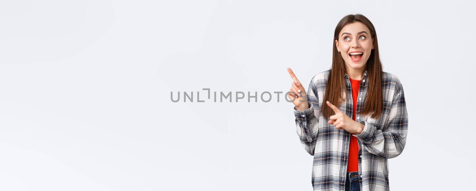 Lifestyle, different emotions, leisure activities concept. Excited happy woman in checked shirt pointing fingers upper left corner and smiling amused, making choice, found what she look for by Benzoix