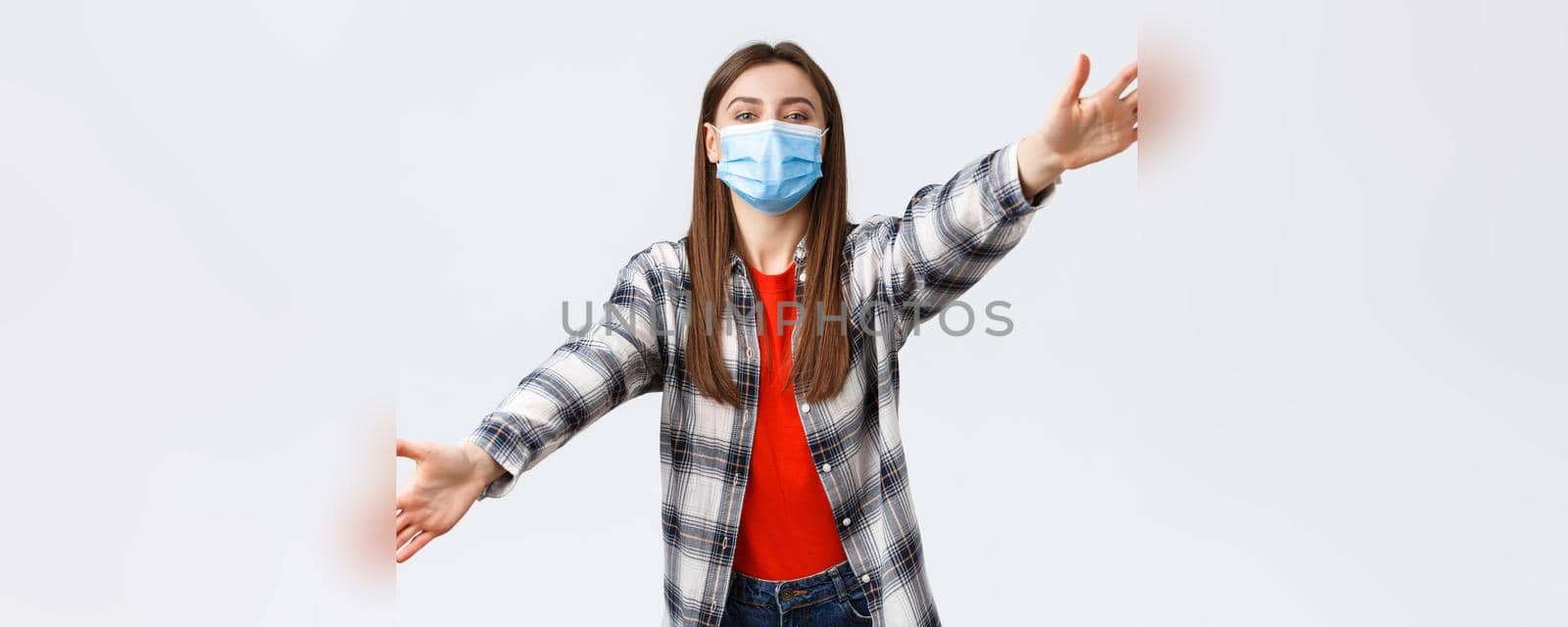 Coronavirus outbreak, leisure on quarantine, social distancing and emotions concept. Cute young woman in medical mask on self-isolation with family, spread hands sideways, dreaming of hugging you.