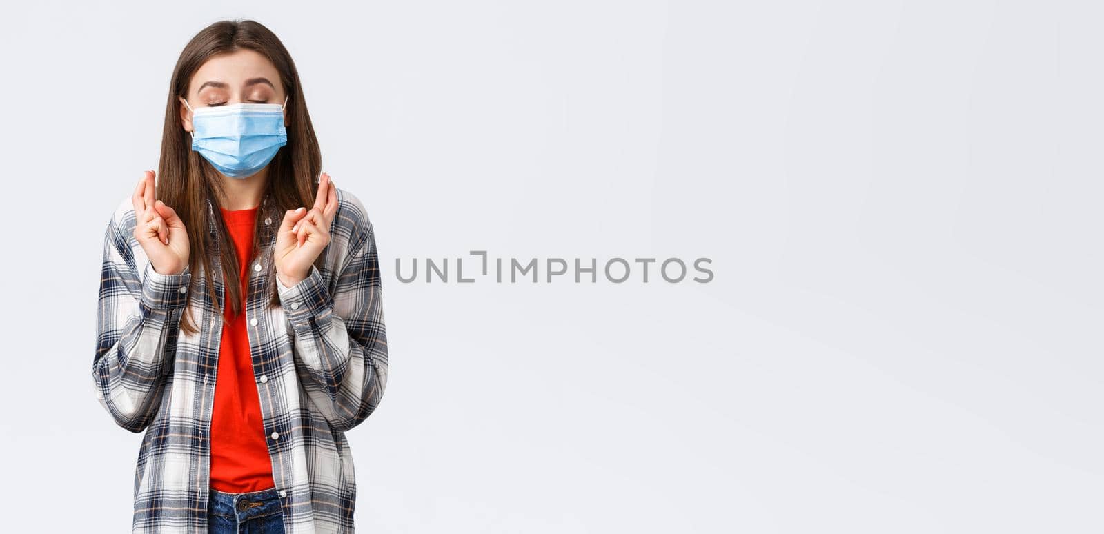 Coronavirus outbreak, leisure on quarantine, social distancing and emotions concept. Hopeful cute young woman in medical mask praying, close eyes and cross fingers good luck, making wish by Benzoix