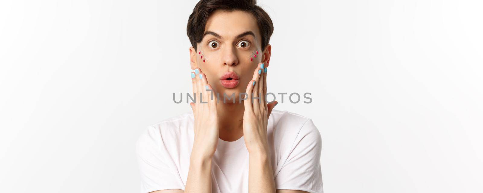 People, lgbtq and beauty concept. Close-up of handsome gay man express surprise, showing hands with blue nail polish, standing over white background.