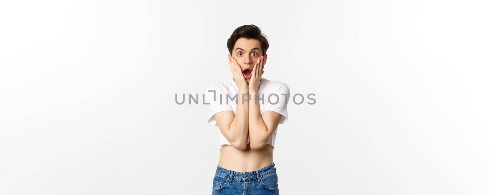 Lgbtq and pride concept. Image of surprised androgynous guy gasping amazed and staring at camera in awe, standing over white background.