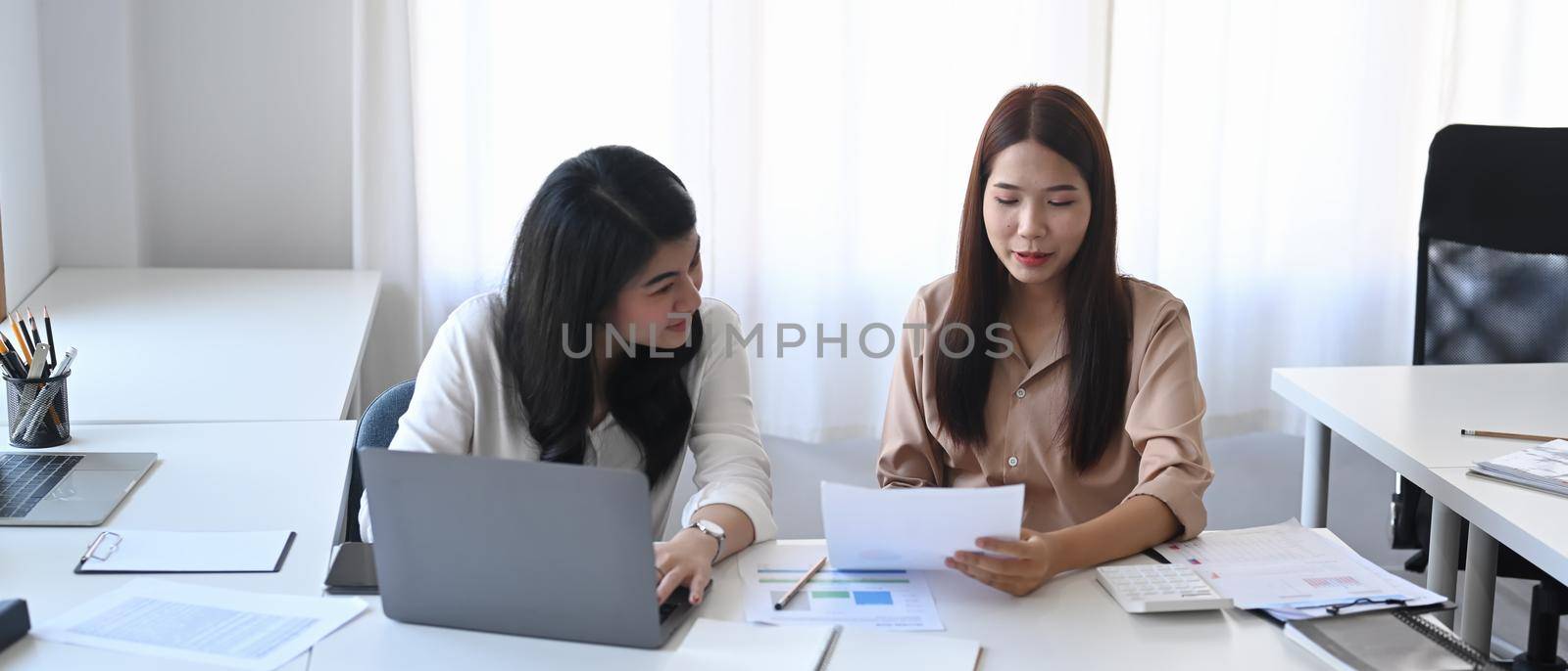 Two young business colleagues discussing their new project together. by prathanchorruangsak
