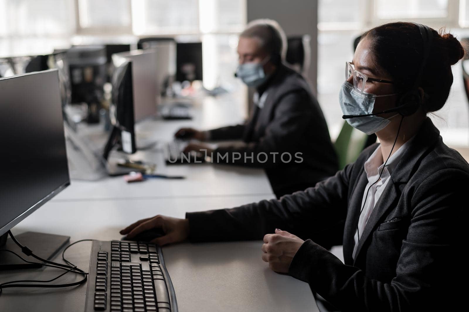 Two women in medical masks and headsets are working in the office.