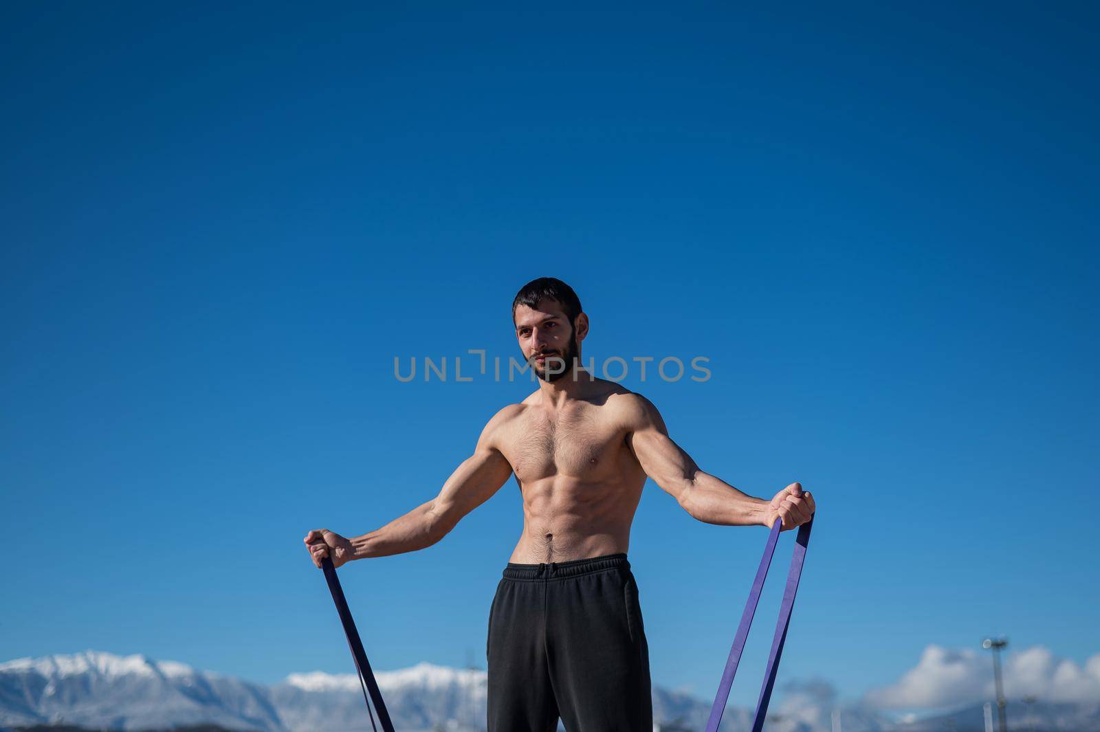 Shirtless man doing exercise with rubber bands outdoors