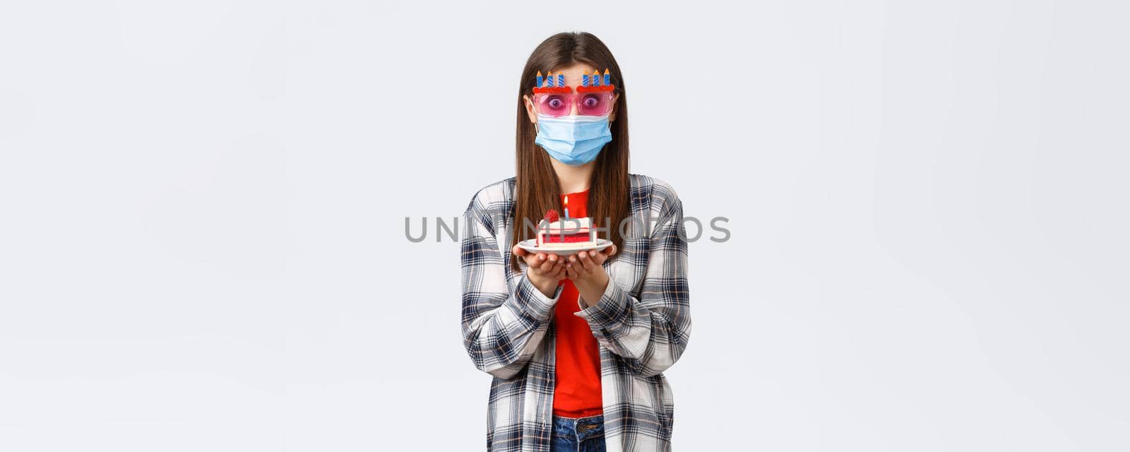 Coronavirus outbreak, lifestyle during social distancing and holidays celebration concept. Surprised or ambushed cute girl in glasses and medical mask, holding birthday cake, confused how blow candle by Benzoix