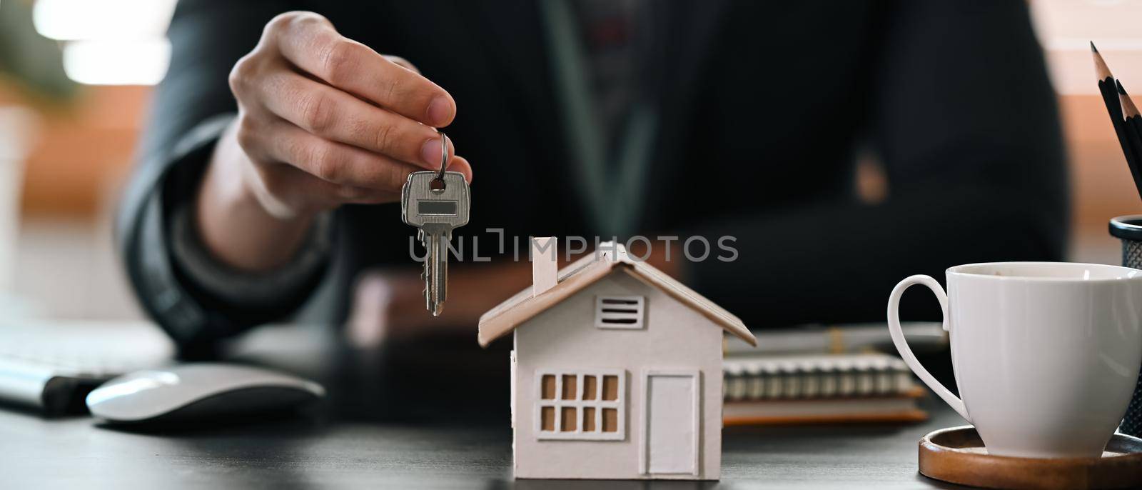 Cropped shot real estate agent holding house key. Insurance or loan real estate concept. by prathanchorruangsak