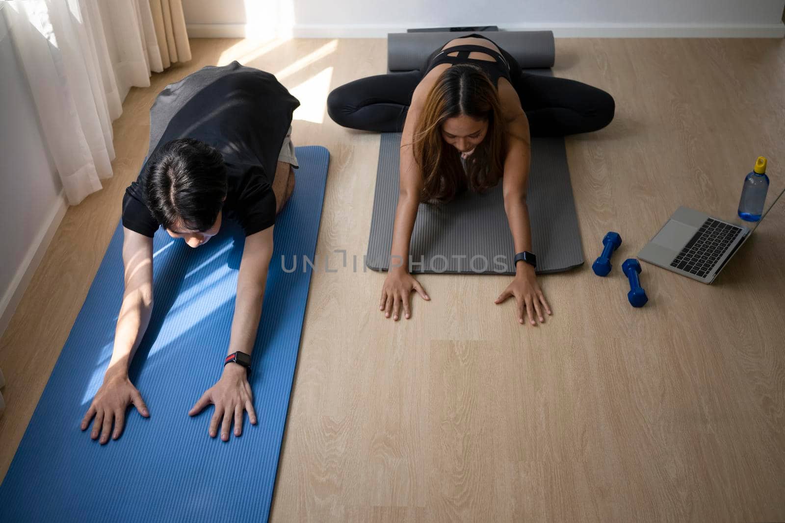 Young healthy couple practicing yoga with online class from laptop in a bright living room.