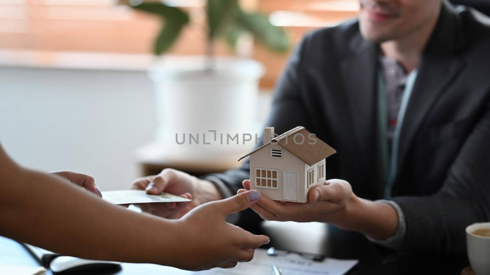 Cropped image of male estate agent holding house model and give proposal to customer. by prathanchorruangsak