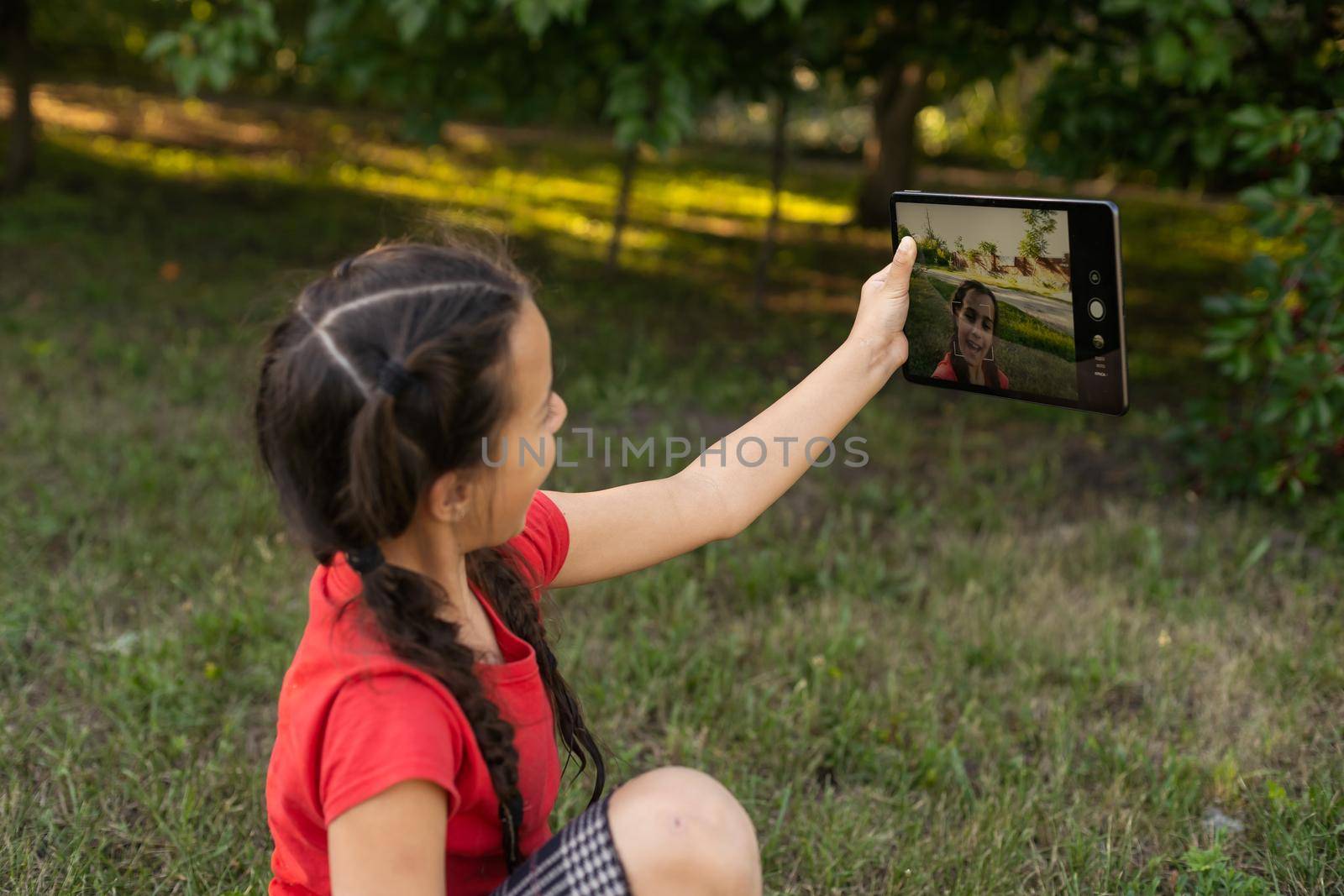 Child girl playing on a Digital tablet in the garden. Online or Remote education concept by Andelov13