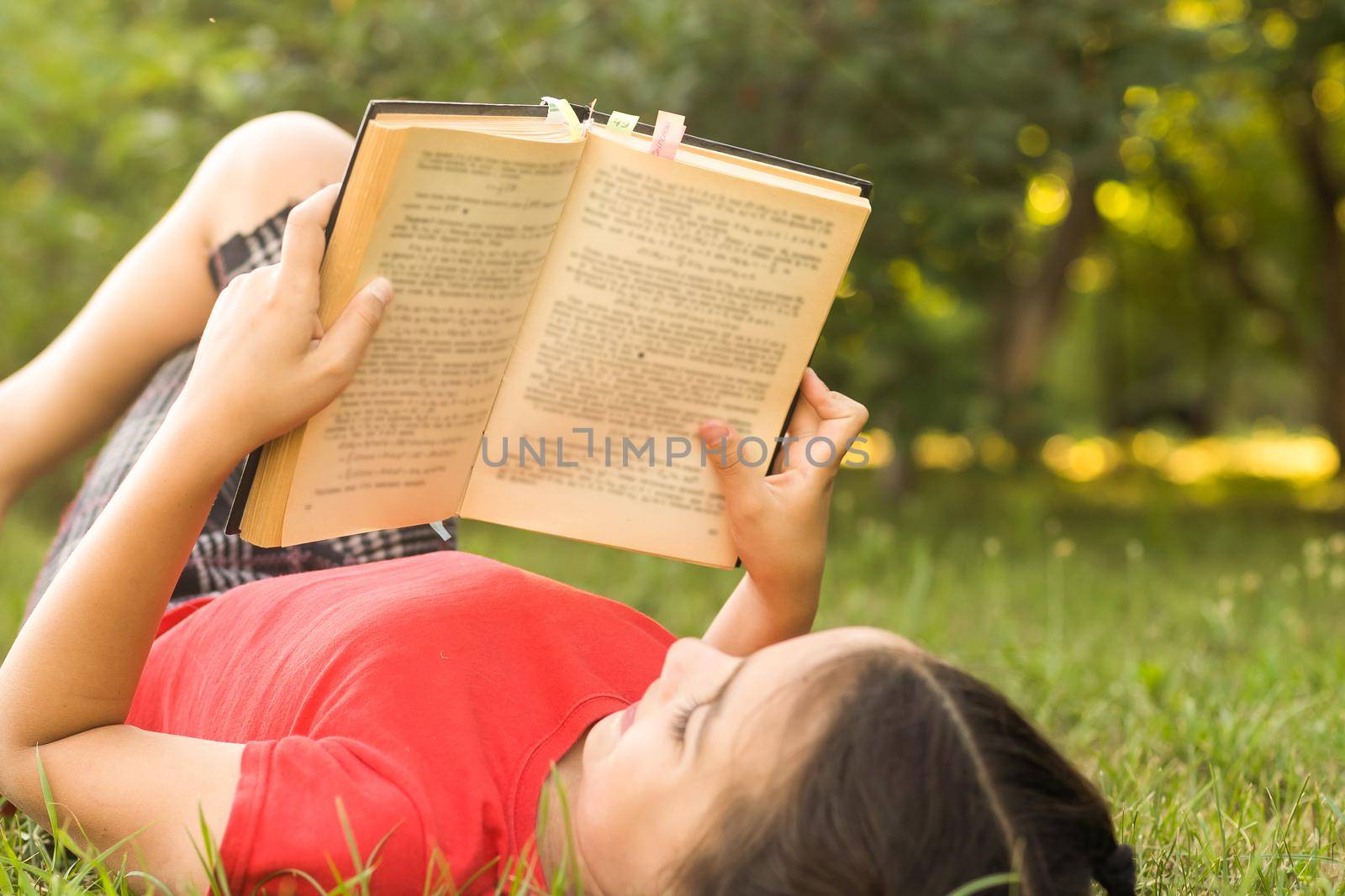 Little girl with a book in the garden. Kid is readding a book on hands. outdoors in summer day. Countryside by Andelov13