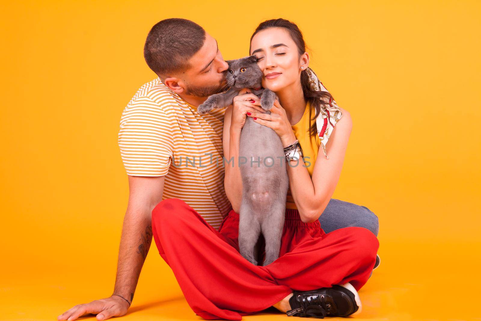 Beautiful young couple sitting down on studio and loving their adorable cat. Couple enjoying time with their cat.