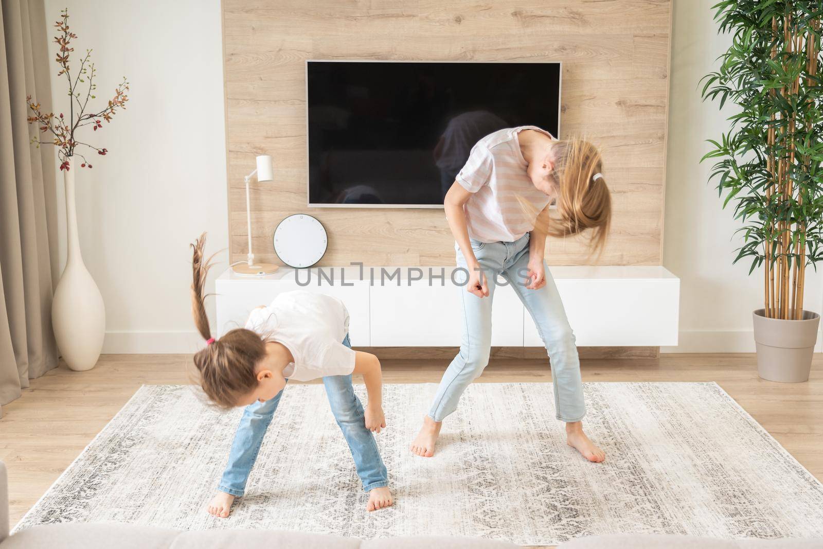 Two sisters having fun dancing in living room, happy family concept by Mariakray
