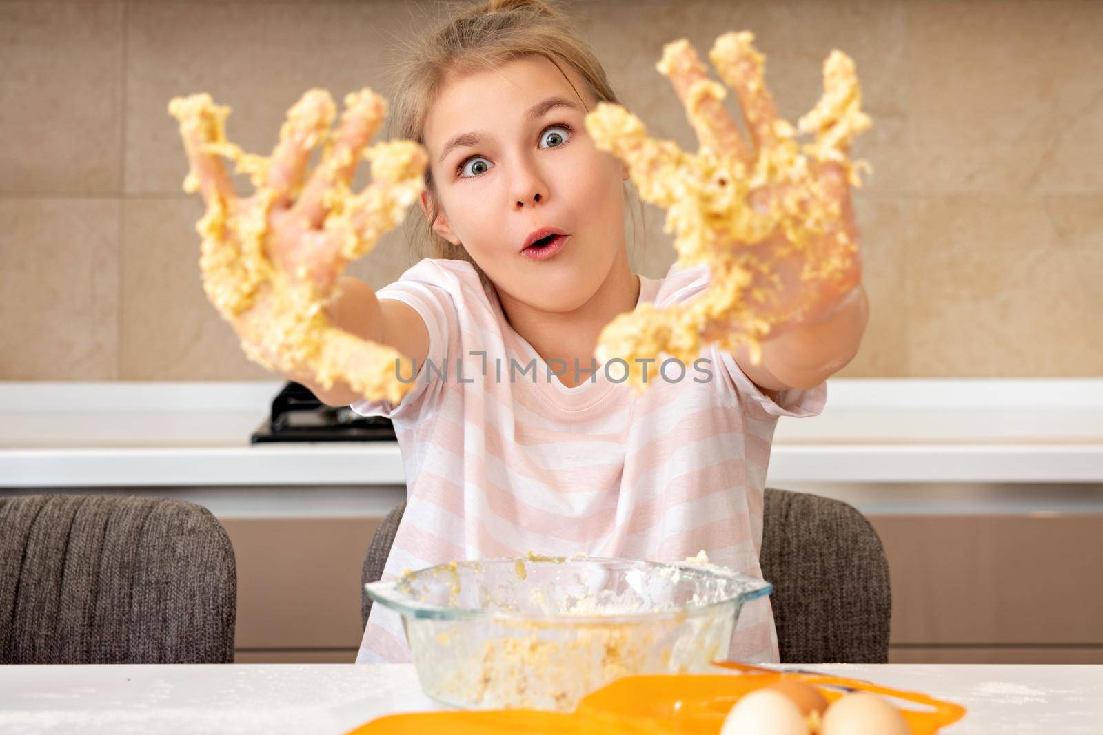 Portrait of a little girl in the kitchen dressed as a professional cook playing with flour, gets her hands dirty and smiles happy. Concept of: nutrition, cooking school, education and game.