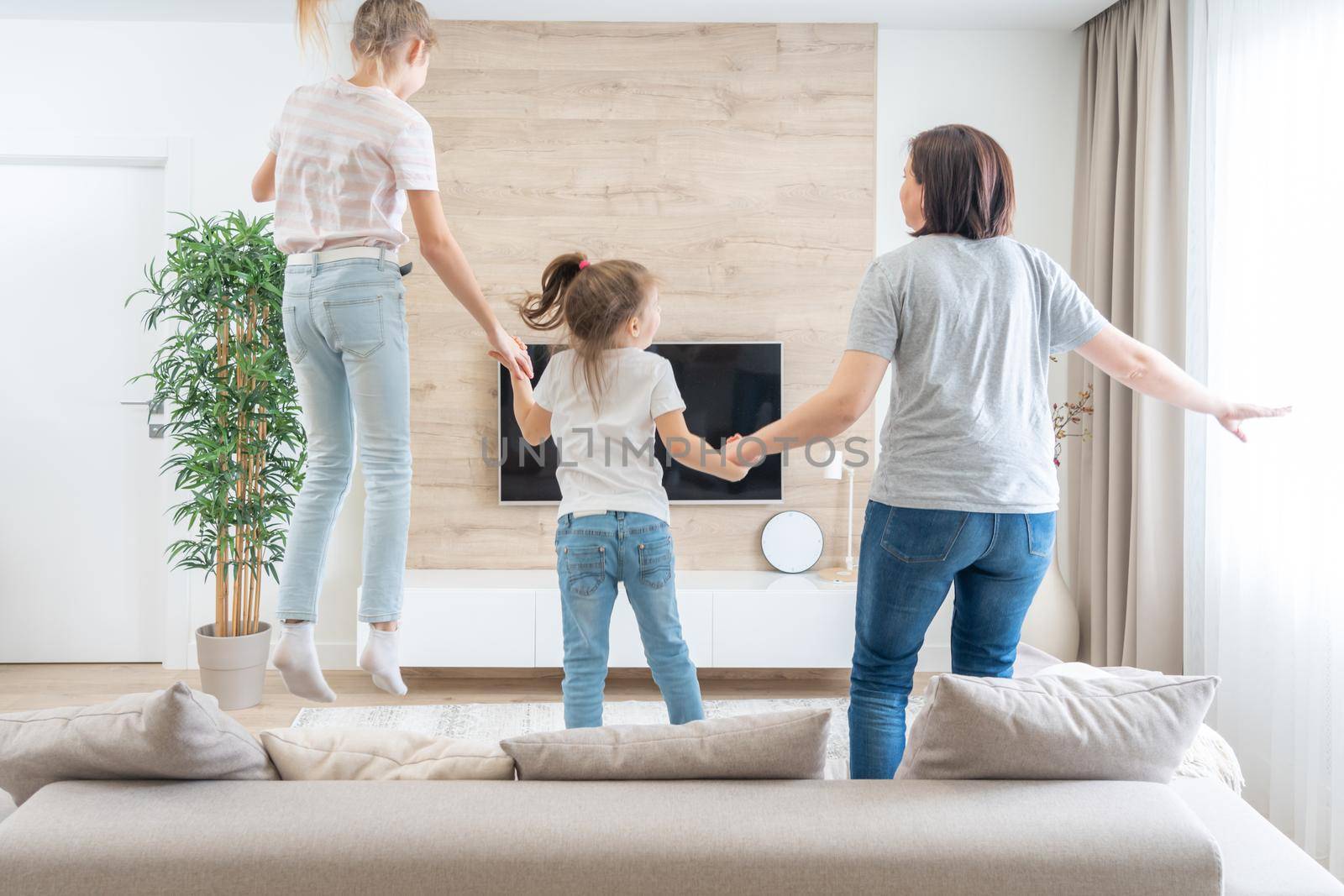 Mother and two daughters having fun jumping on sofa in living room