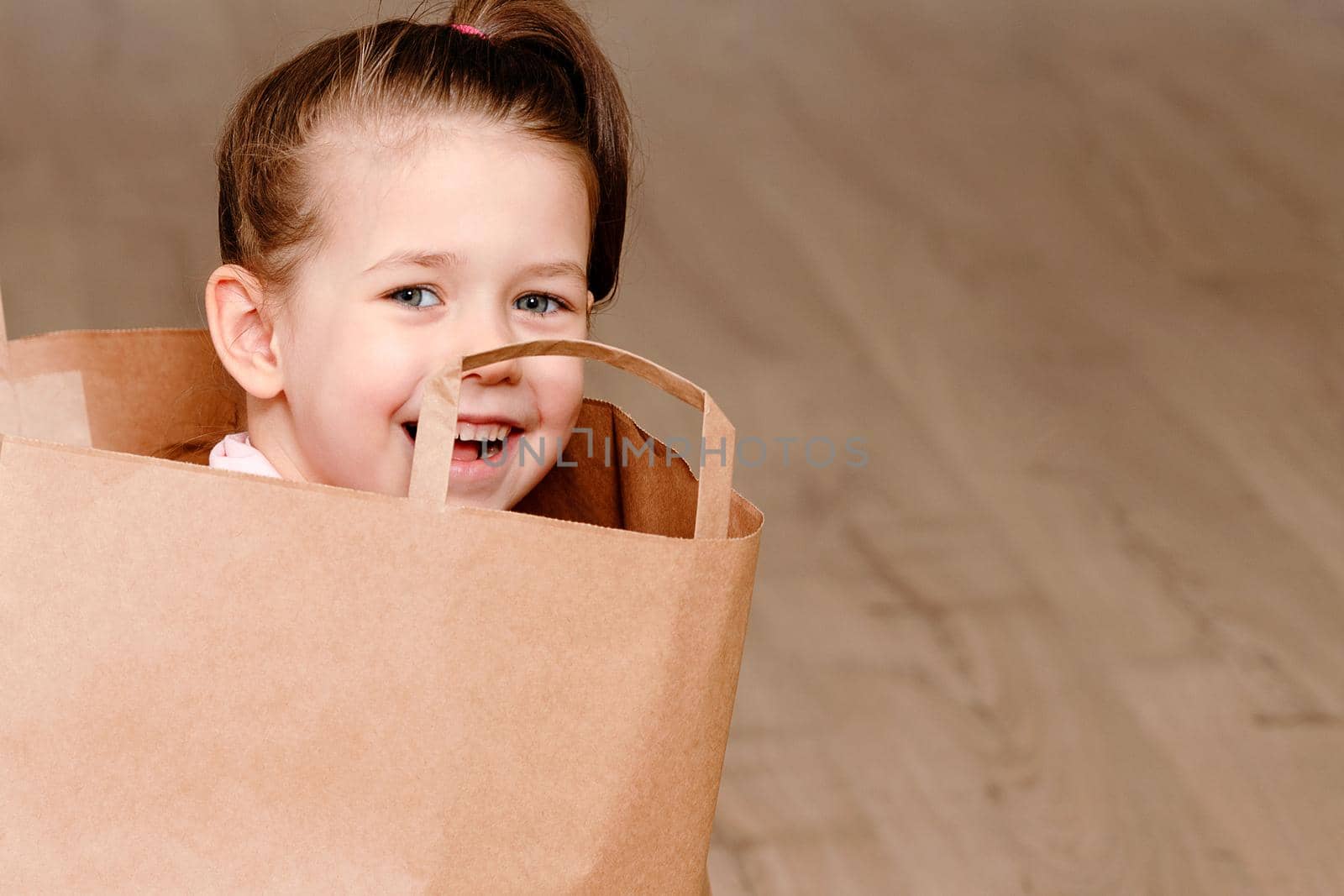 Little girl sitting in Brown paper shopping bag