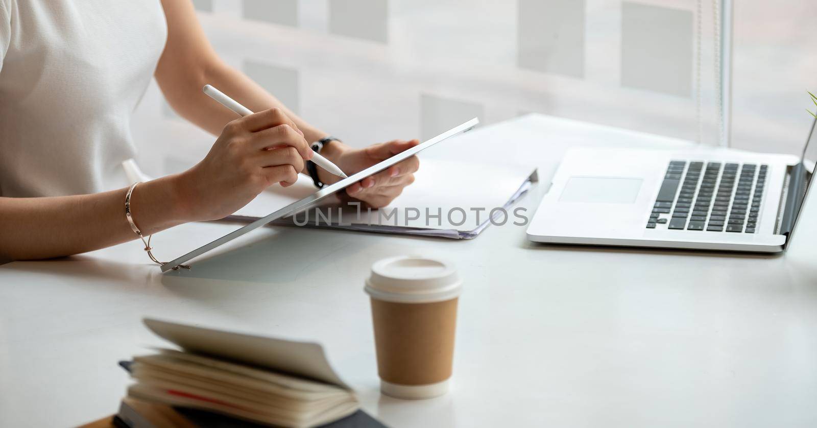 Young business woman hands holding pen stylus and working on black digital tablet pc with laptop computer on the desk at modern home office. Remote working, online learning concept by nateemee
