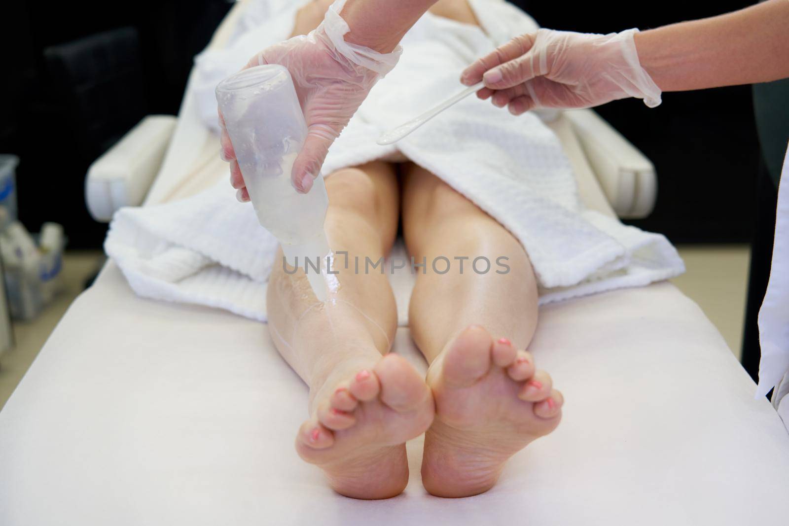 Cosmetologist preparing female patient for laser hair removal on legs in spa salon by Mariakray