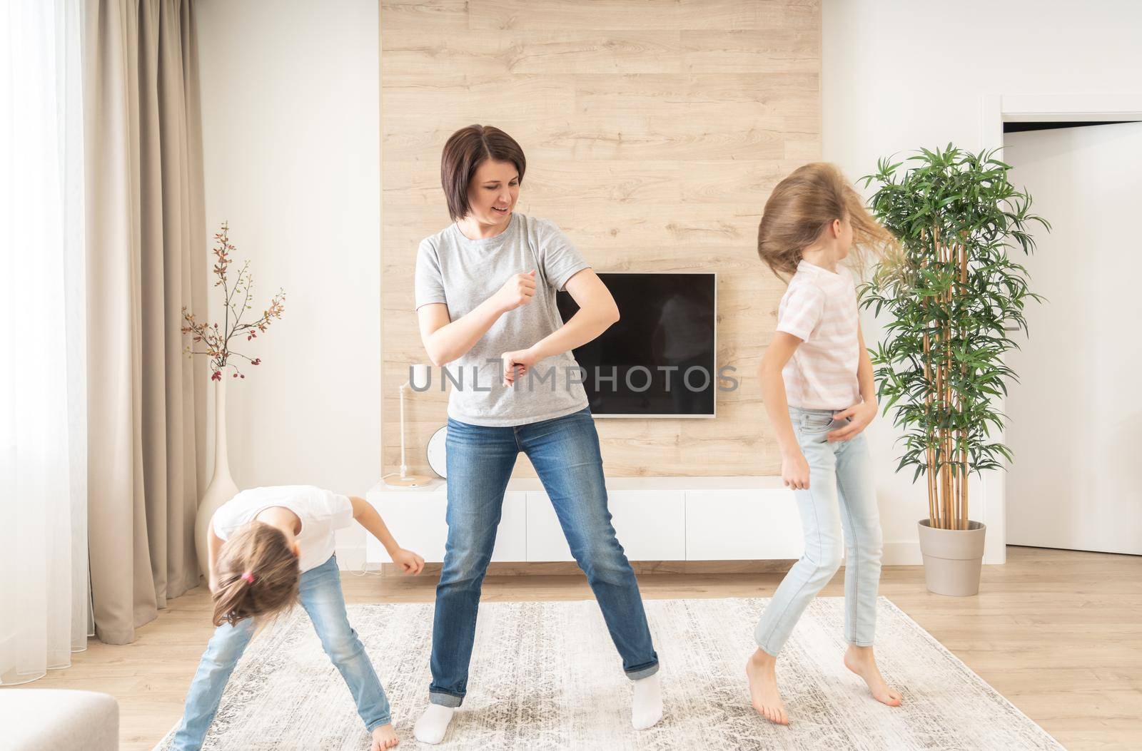 Happy mother and two daughters having fun dancing in living room. mother laughing enjoying funny lifestyle activity with teenage girl at home together. by Mariakray