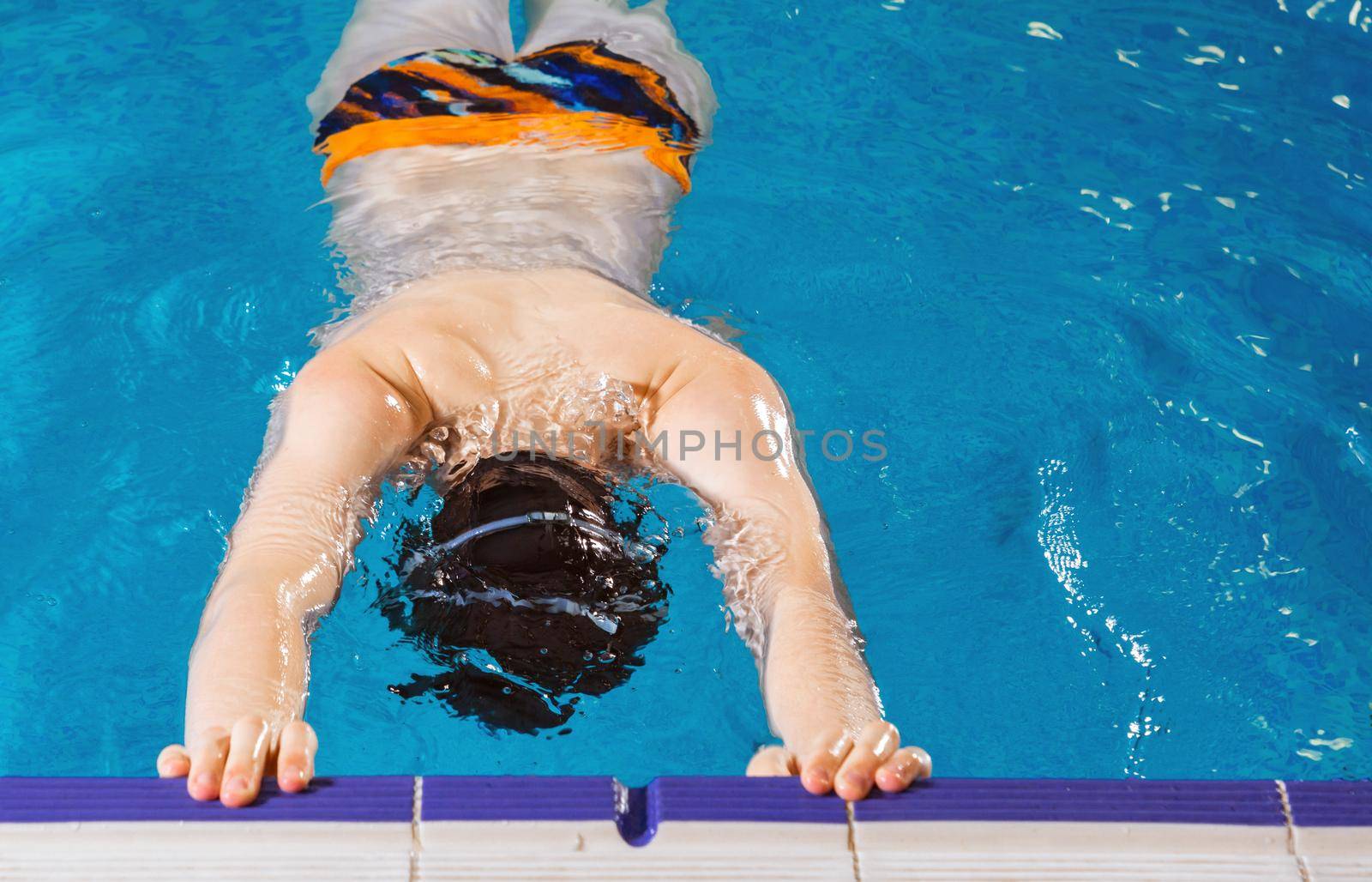 Preteen boy swimming in indoor pool during swim class by Mariakray