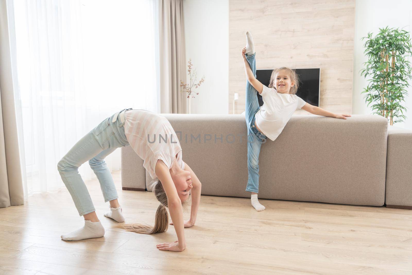 Two girls doing stretching exercises in living room at home by Mariakray