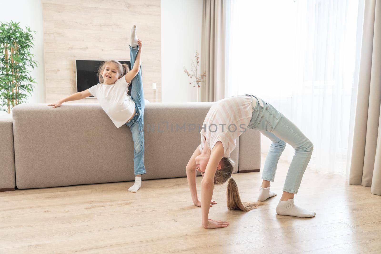 Two sisters doing yoga stretching exercises in living room at home
