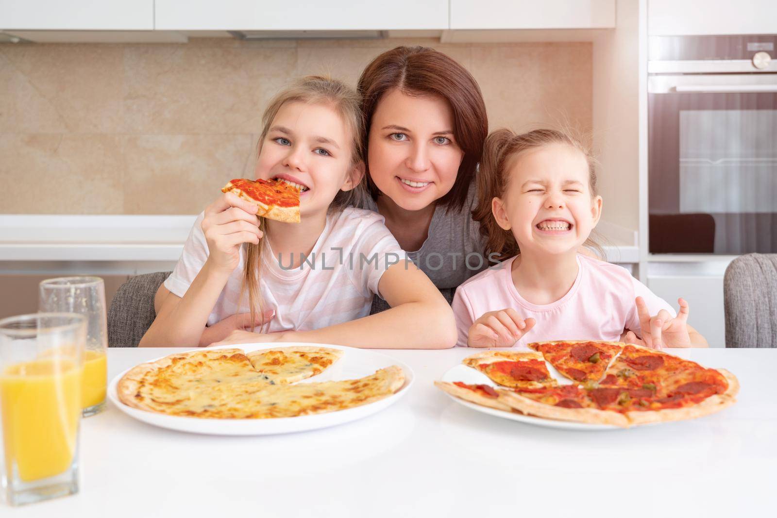 Mother and two daughters eating homemade pizza at a table in kitchen, happy family concept by Mariakray