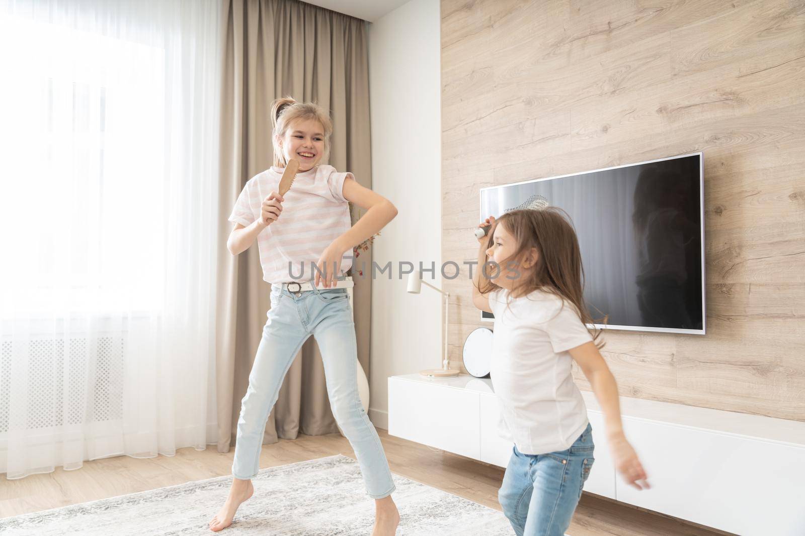 Two sisters having fun dancing in living room and singing karaoke, happy family concept by Mariakray