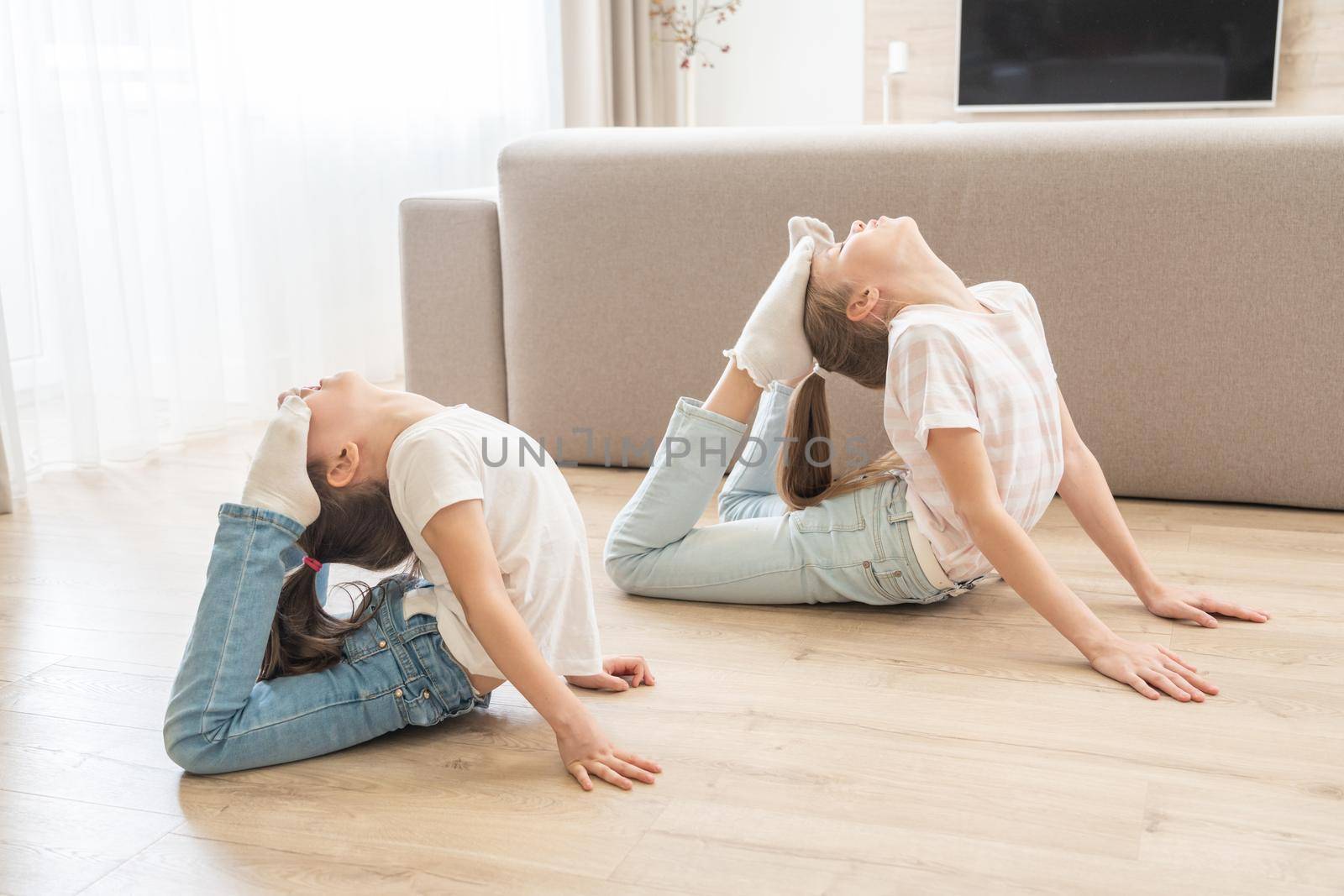 Two girls sisters practicing yoga at home, stretching in King Cobra pose by Mariakray