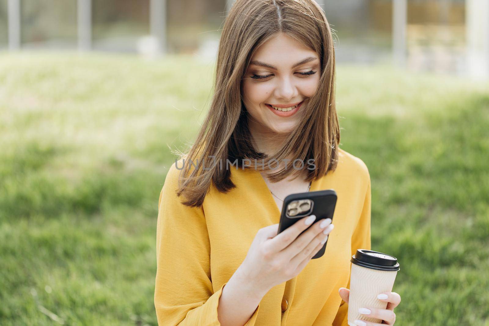 Business woman typing message on mobile phone near office. Young girl chatting on phone. Young woman hands using smartphone on bench near modern buildings by uflypro