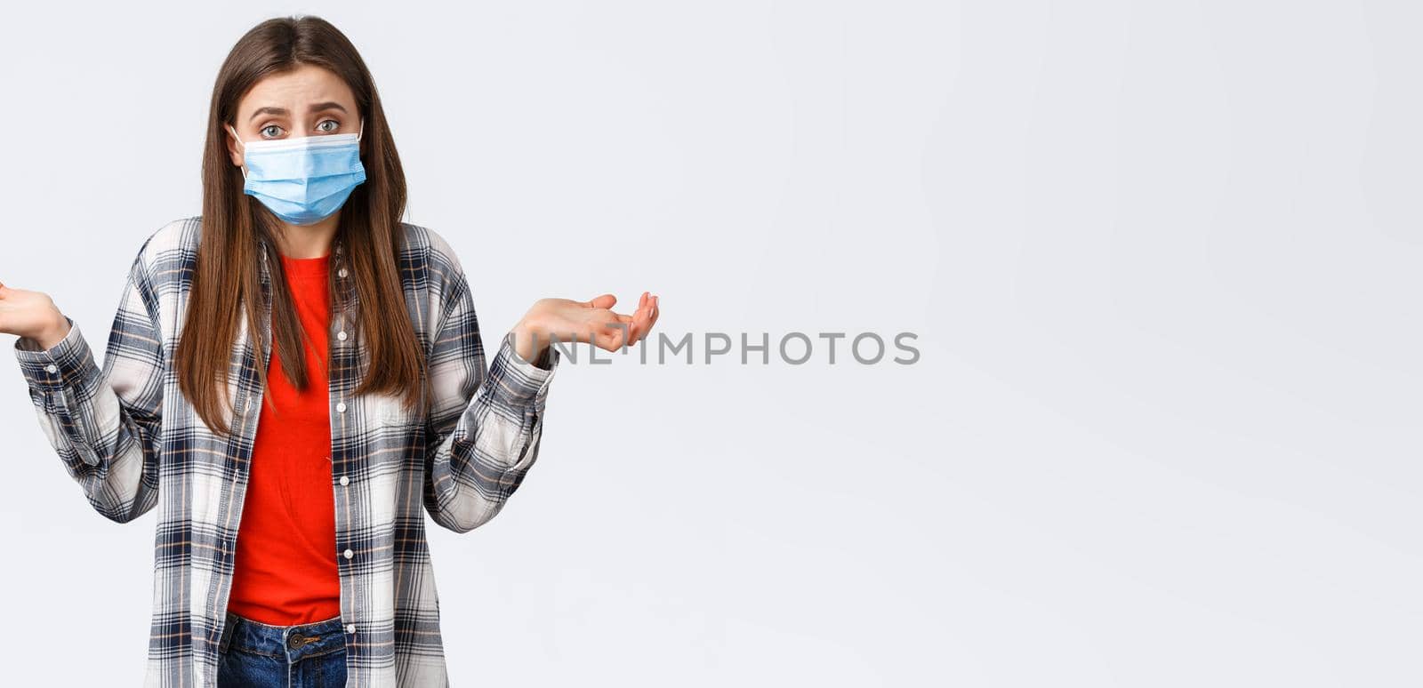 Coronavirus outbreak, leisure on quarantine, social distancing and emotions concept. Confused and indecisive young woman in medical mask dont know what do, shrugging with hands spread sideways.