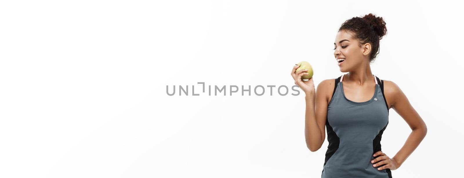 Healthy and Fitness concept - Beautiful American African lady in grey fitness clothes holding green apple. Isolated on white background