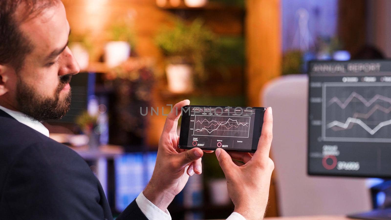 Close up as a businessman looks at some graphics on the smartphone screen. Office background
