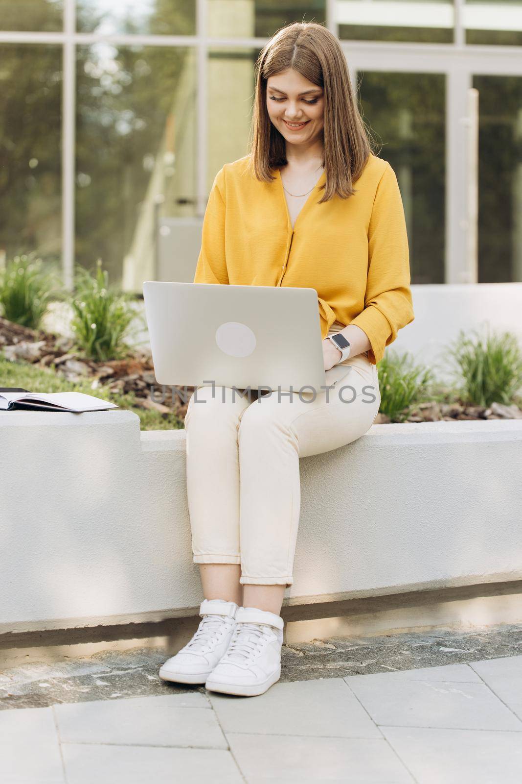 Focused business woman entrepreneur typing on laptop doing research. Young female professional girl using computer sitting outside office. Busy worker freelancer working on modern tech notebook device