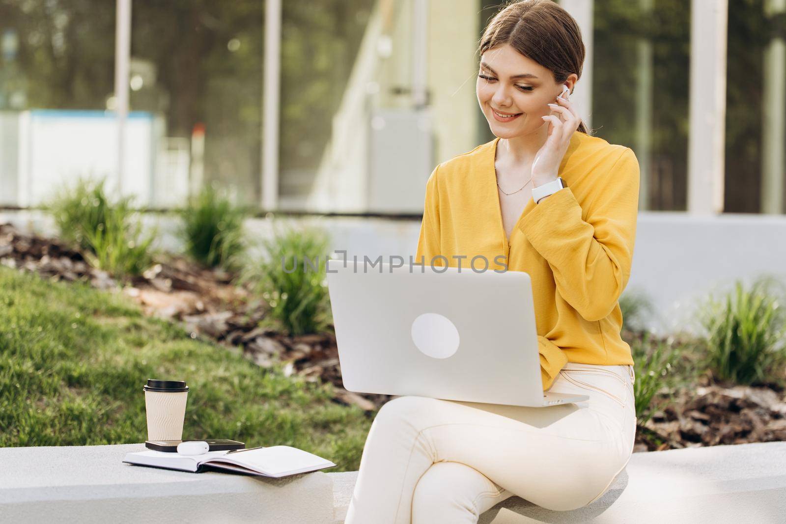 Portrait of attractive woman using laptop in coworking space. Young woman wearing earphones sitting in front open laptop computer and looking ahead. Study, remote work, learning, freelance.