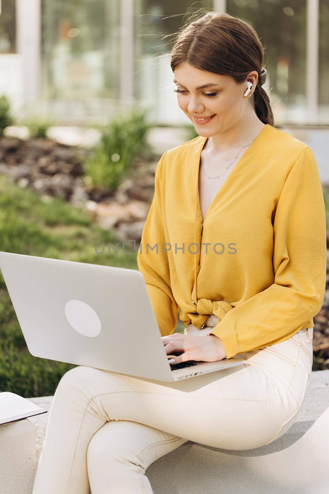Young woman wearing earphones sitting in front open laptop computer and looking ahead. Portrait of attractive woman using laptop in coworking space. Study, remote work, learning, freelance.