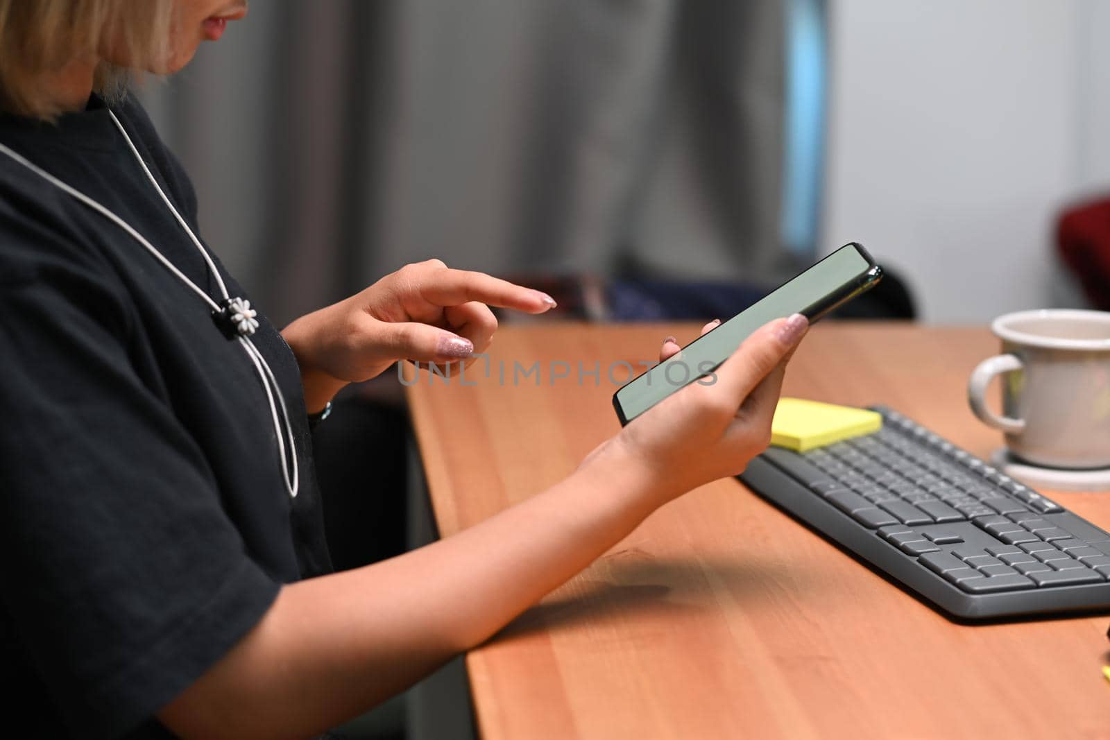 Side view young woman using smart phone while sitting at her workplace.